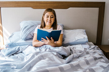 latin middle aged woman reading a book in bed at home in Latin America