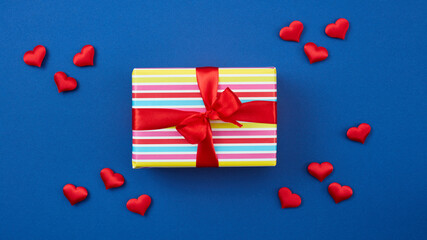 wrapped gift box with red ribbon and hearts on blue background