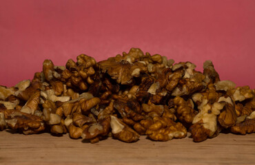 Walnuts on a wooden table with a pink background.