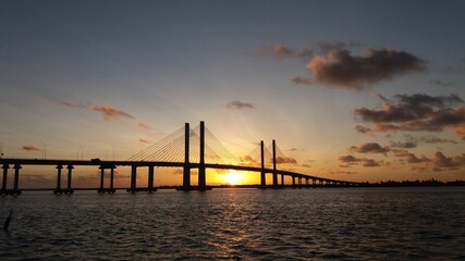 Fototapeta na wymiar Nascer do sol por trás de uma ponte que atravessa um rio.
