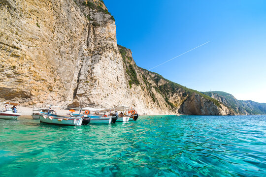 Boats line up at the shoreline in the clear waters off the sandy Paradise Beach or Chomi Beach on a sunny day in Corfu Greece.