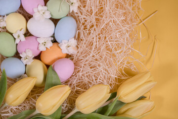 multicolored easter eggs on hay and near yellow tulips on yellow background