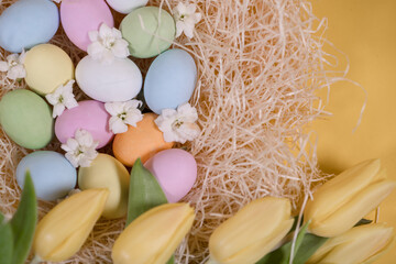 multicolored easter eggs on hay and near yellow tulips on yellow background