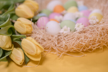 multicolored easter eggs on hay and near yellow tulips on yellow background