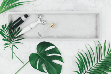 Facial roller from crystal rose quartz and massage tool jade Gua sha on the tray on grey background with palm leaves. Tools for anti-age massage, natural face lifting at home.	