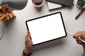 Overhead shot of man holding mock up digital tablet with blank screen on white office desk.