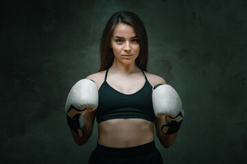 Fototapeta na wymiar Young angry fighter girl with white gloves fighting practice throwing aggressive punch training shadow boxing workout on black dirty grunge background