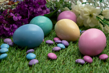 Pastel colored Easter eggs and pastel colored chocolate candy on green grass 