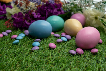 Pastel colored Easter eggs and pastel colored chocolate candy on green grass 