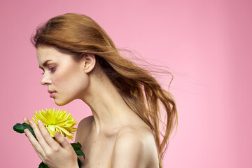 Beautiful girl with a yellow flower on a pink background nude shoulders makeup