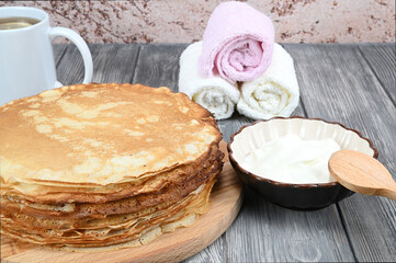 A stack of pancakes, a mug of tea, a saucer of sour cream and a few napkins.