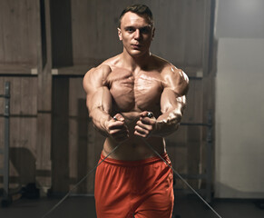 Young handsome sporty bodybuilder exercising with stretching band in gym