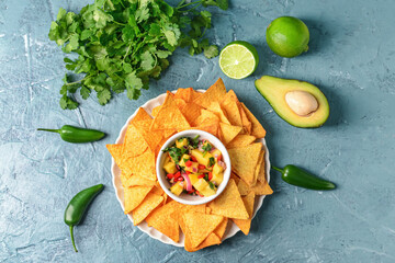 Plate with fresh mango salsa and nachos on color background