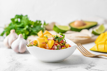 Bowl with fresh mango salsa on light background, closeup