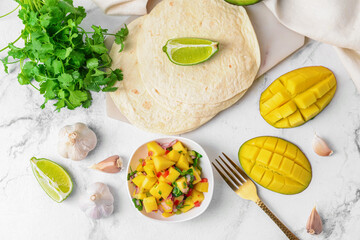Composition with fresh mango salsa and tortillas on light background