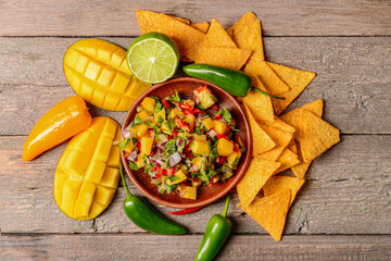 Plate with fresh mango salsa and nachos on wooden background