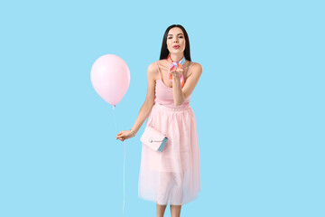 Beautiful young woman with balloon blowing kiss on color background
