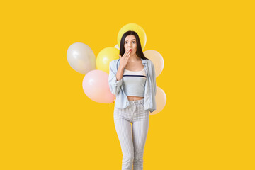 Surprised young woman with balloons on color background