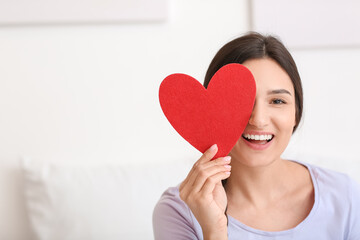 Beautiful young woman with red heart at home