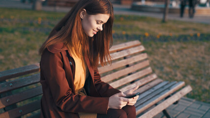 woman in the park sitting on a bench with a phone in her hands chatting outdoors