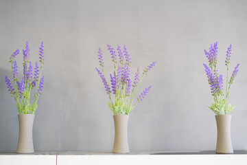behind a gray background, in front there are three vases with lavada branches