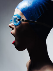 Side view of a woman in a blue swimming cap and glasses on a gray background
