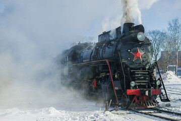 Fototapeta na wymiar Old freight steam locomotive in the clouds of steam on a frosty day. Russia