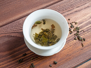 green tea is brewed in a white bowl on a wooden background. Dry tea leaves lie nearby. Top view