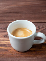 a white cup with a delicious and aromatic espresso on a wooden background. Vertical photo, side view
