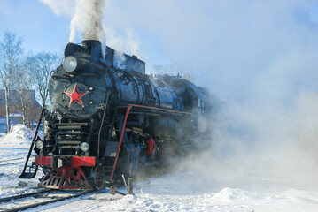Fototapeta na wymiar Old Soviet steam locomotive in the clouds of steam on a frosty winter day. Russia