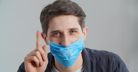 Portrait of young adult caucasian man showing how to properly wear medical mask on his face puts on respirator on mouth waving finger negatively saying no closes nose showing thumbs up, hygiene rules