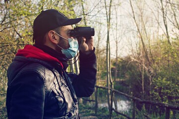 Middle age man observing in the nature wearing a surgical mask , concept of bird watching during Corona Virus