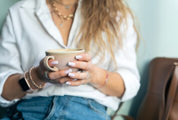 Well dressed woman with different accessories on her hands. Holding cup of coffee at the morning