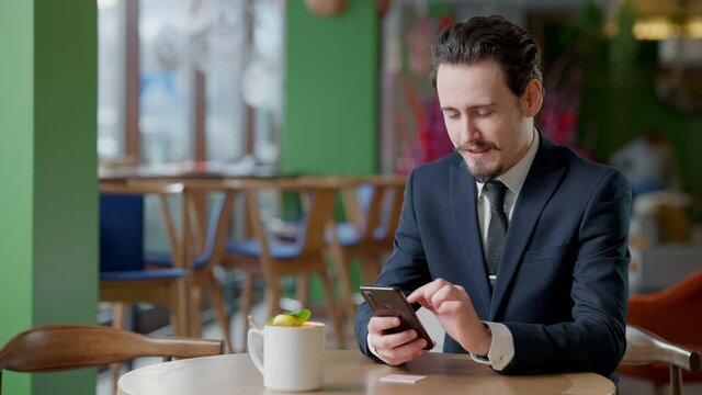 Confident modern man scanning QR code with smartphone in cafe. Portrait of brunette handsome bearded businessman with mustache using online menu in restaurant. Modern lifestyle.