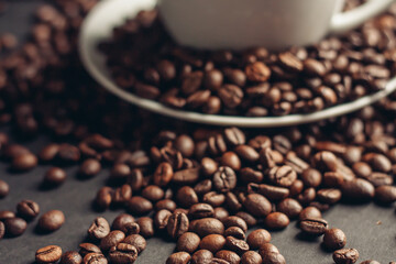 saucer with coffee beans and white cup on gray table close-up