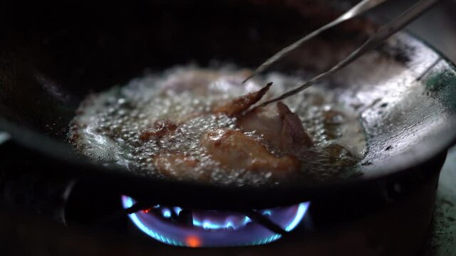 chicken meat cooking in hot oil on pan, unhealthy of fatty to people, splash and droplet of oil danger, gas fuel burnning to heat for fried or roast meat, raw fried chicken drumstick menu of delicious