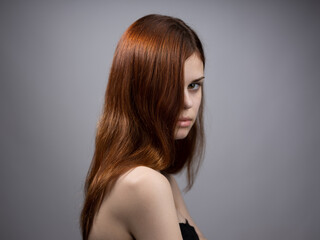 Fototapeta premium Beautiful woman with loose red hair on a gray background bared shoulders portrait