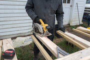 Closeup of a carpenter cutting a wood plank with a chainsaw.