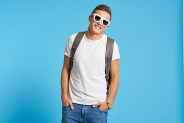 Cheerful young guy with backpack studio blue background