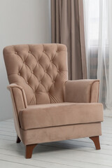 a classic beige armchair stands in the room near the window. Curtains and tulle hang behind it. Modern and elegant interior design