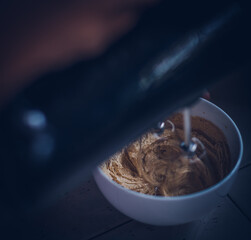 Making famous Korean beverage also known as Dalgona coffee, whisking instant coffee in a bowl with an electric beater in the home kitchen, sugar water coffee mix in same quantities for prepare frost.