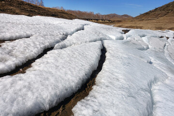 Snow in the mountains melts in the spring. Layers of snow descend in parts from the slope. Natural background.