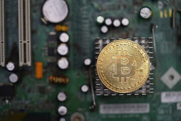 Gold bitcoin coin on top of motherboard heatsinks components showing cryptocurrency core.