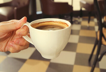 Man's hand holding a cup of hot coffee with blurry room in background