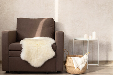 A sheep skin on a chair, next to a wicker basket with a blanket and a coffee table with candles.
