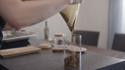 man chocolate granola pour into glass beaker jar on concrete countertop