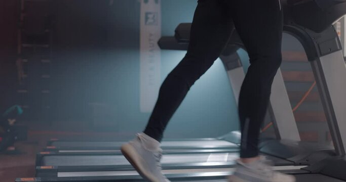Close up view of man legs in sneakers running on treadmill at gym, slow motion