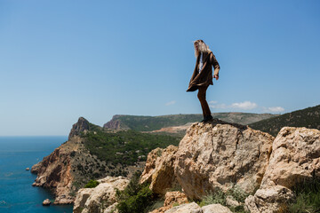 fellow hipster with long blond hair stands on top of a hill in the wind in sunny summer weather. High quality photo