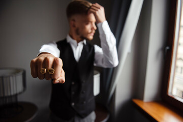 Handsome groom in stylish suit holding wooden cufflinks