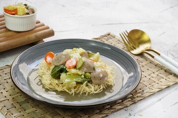 A plate of I Fu Mie or Crispy Fried Noodle with thick savory sauce and meatball and vegetables in shiny and grainy white background. Selective focus